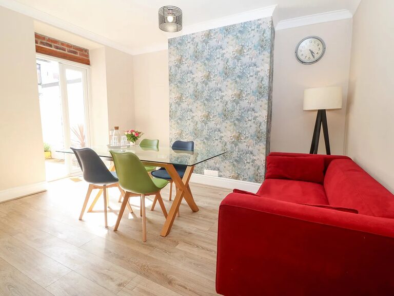 Dining area with glass table and red sofa at the 5-Bed House, large group holiday home in Llandudno